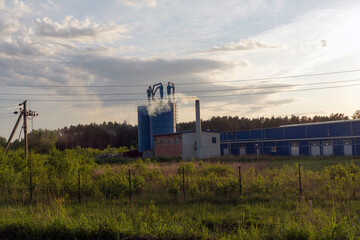 Factory in the field. Two large tanks and a pipe from which smoke comes.