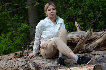 Outdoor close up portrait of young beautiful woman coat,sitting on a tree stump, Trees Chopped And Stacked In Forest
