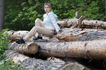 Outdoor close up portrait of young beautiful woman coat,sitting on a tree stump, Trees Chopped And Stacked In Forest