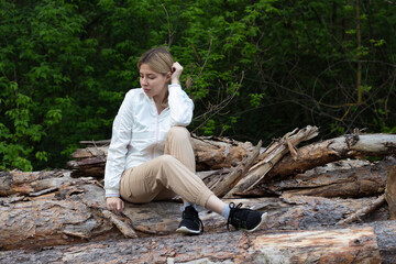 Outdoor close up portrait of young beautiful woman coat,sitting on a tree stump, Trees Chopped And Stacked In Forest