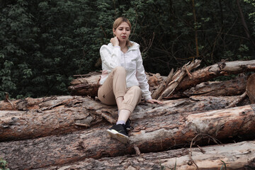Outdoor close up portrait of young beautiful woman coat,sitting on a tree stump, Trees Chopped And Stacked In Forest