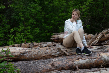 Outdoor close up portrait of young beautiful woman coat,sitting on a tree stump, Trees Chopped And Stacked In Forest
