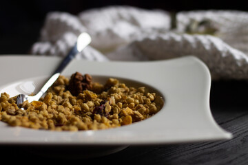 Cereal granola in a white plate with a spoon on a black wooden tabletop.