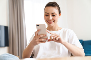 Photo of woman using mobile phone and smiling while sitting on chair
