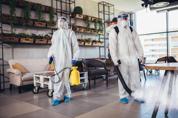 Professional workers in hazmat suits disinfecting indoor of cafe or restaurant, pandemic health...