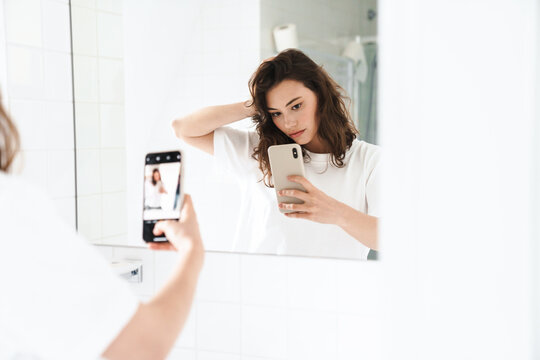 Photo of woman taking selfie on cellphone while looking at mirror