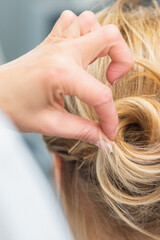 Close up rear view of hairdresser making hairstyle for long hair of blonde woman.