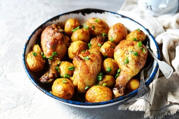 Baked chicken legs with young potatoes in a baking dish on a gray background