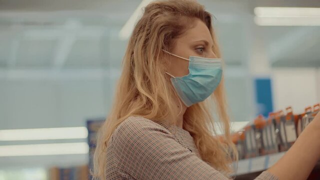 Woman Shopper Choosing Product In Hypermarket Store.Girl In Face Mask Shopping In Market On Covid19 Coronavirus Pandemic Quarantine Lock down. Bayer In Medical Mask In Supermarket Avoid Self Distance