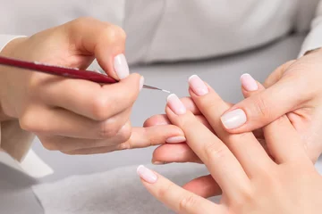 Tuinposter Hand of young woman receiving french manicure by beautician at nail salon. © okskukuruza