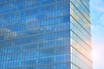 Facade texture of a glass mirrored office building. Fragment of the facade. Bottom view of modern skyscrapers in business district in evening light at sunset with lens flare filter effect.