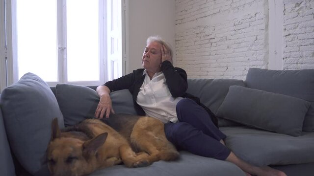 Depressed senior old woman crying on couch with pet dog as only Companion. Sad and tired widower amid COVID-19 pandemic. Coronavirus death, lockdown, social distancing and Mental health.