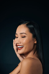 Fototapeta premium Beautiful young woman in lace top with red lips touching face. Over black background. Copy space.