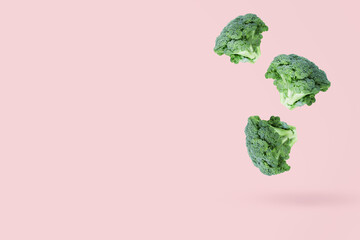 Three broccoli heads fall freely on a pink background casting a light shadow. Creative flying food concept.Minimalistic vegetable background with free copy space for text.