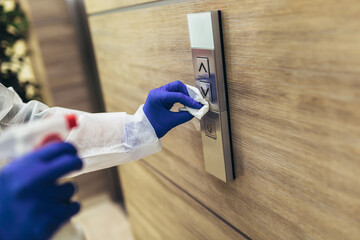 Staff using disinfectant from the bottle spraying an elevator push button control panel....