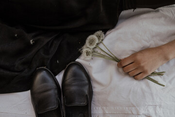 In a female palm, dandelions, next to a black dress and a pair of shoes on a beige fabric