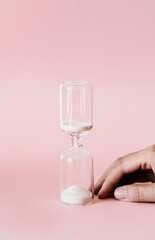 Hourglass on pink and white background, sand flowing through the bulb of sandglass measuring time. minimal concept.