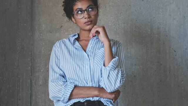 A pretty nice young african businesswoman is thinking about something and then come up with a good idea while raised her finger up standing over gray concrete wall