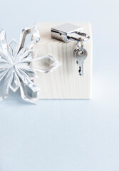 Silver shiny metal padlock with keys and glass snowflake on wooden stand and blue background. 