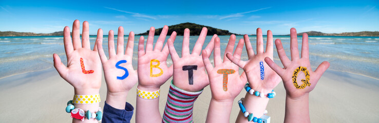 Children Hands Building Colorful German Word LSBTTIQ Means LSBTQ. Ocean And Beach As Background