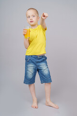 Smiling boy standing with fruit orange and drink. Isolated on gray