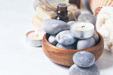 Fototapeta na wymiar Spa composition with essential oil, stones, soft towel, candle. Aromatherapy and relax, atmosphere of serenity and relaxation. Close up, macro view. White wooden background, copy space for text