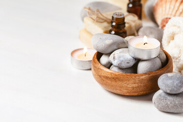 Fototapeta na wymiar Spa composition with essential oil, stones, soft towel, candle. Aromatherapy and relax, atmosphere of serenity and relaxation. Close up, macro view. White wooden background, copy space for text