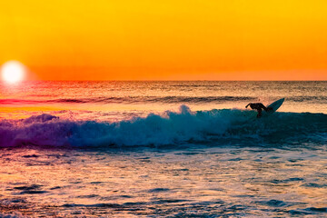 The silhouette of a surfer riding a wave at an empty surf spot. Young surfer rides the wave during sunset. Image