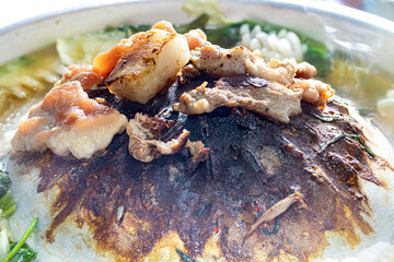 A preparation of roasted meat with sauce of vegetable on Hot Pot - Mu Kratha, close up..Grilled slice pork at Thai Barbecue style with smoke around.