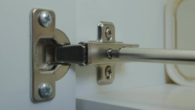 the master twists the adjusting screw of the hinge of the Cabinet door in the kitchen. Installation and adjustment of kitchen Cabinet doors. close-up. 4K