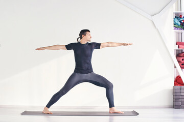 Man stand at warrior pose. Yoga exercise. Inside home online class. Male man at black cloth....
