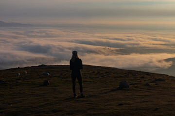 Fototapeta na wymiar Early morning mountain top cloud inversion with young hiker silhouetted enjoying the view, Slieve Meelmore, Mourne Mountains, County Down, Northern Ireland, Area of Outstanding Natural Beauty
