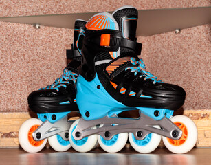 Roller skates on a wooden background. Roller skates are black and blue with orange color.