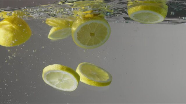 cutted lemons droped into the transparent aquarium with water on grey background Slow motion from 120 fps
