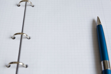 A blue pen lies on a white sheet of a notebook. Open squared school notebook