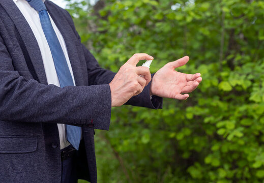 Applying an antibacterial antiseptic sanitizer in male hands of a businessman on nature green blurred background. gel in park for hands disinfection. Outdoor precautionary measures