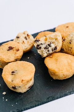 Little chocolate chips muffins with one bitten in a dark slate board plate isolated on white. Muffin, sweet and food concept.
