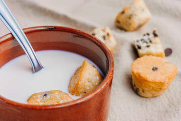 Detail of two mini muffins in a mug with milk and a spoon, with some mini muffins on the background. Selective focus.
