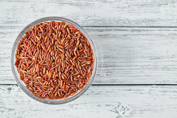 Fototapeta na wymiar Raw red rice grains in a transparent glass plate on wooden background. Closeup, top view