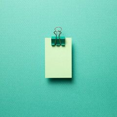 Green memo paper, sticky notes with green binder clip on mint green background. top view, copy space