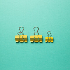 Yellow metal binder clips on mint green background. top view