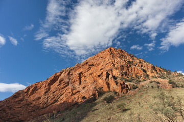 Fototapeta na wymiar Triangle mountain formed by orange and red rock. Green vegetation, cloudy sky. Picture taken during dry season. Simpons gap, West Macdonnell ranges, Northern Territory NT, Australia, Oceania