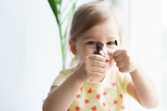 Little Smiling Girl Holding A Medicine Jar Of Iodine And An Ear Stick In Her Hands. Treatment Of Rashes, Acne, Pimples Dermatic Diseases, Contagious Mollusks On Skin In Children. Copy Space.Soft Focus