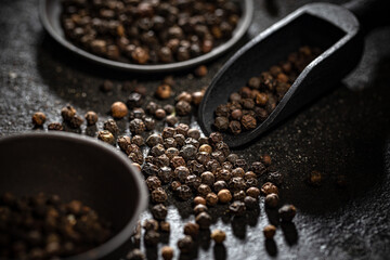 Black peppercorns in black wooden shovel