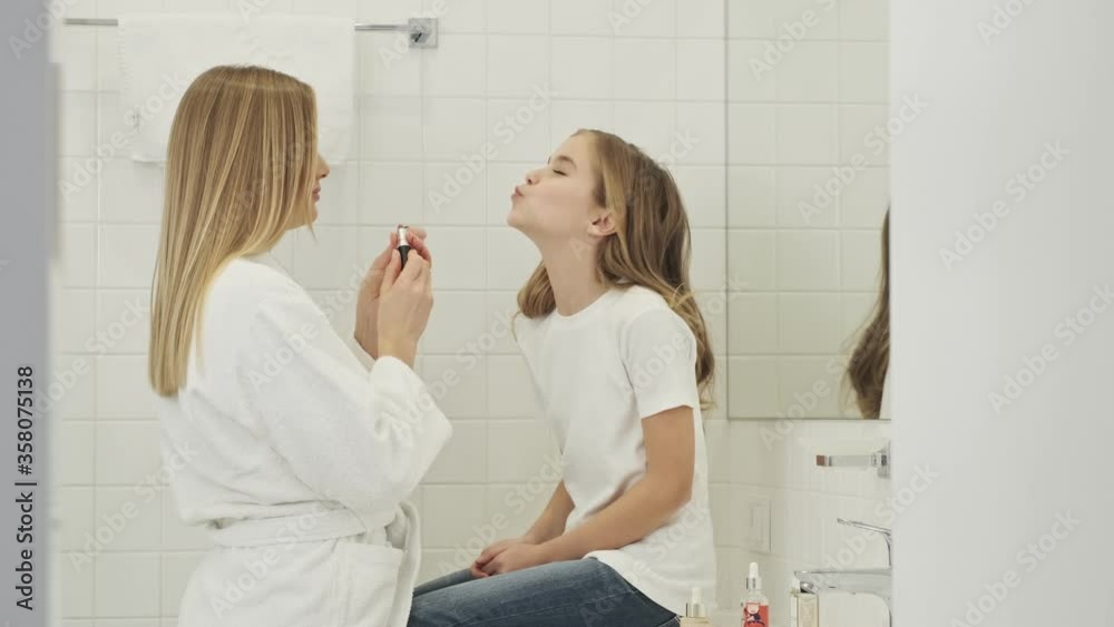 Wall mural a happy young mother is applying lipstick to her little girl in the bathroom in the morning