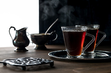 A close up of two steaming cups of tea ready for drinking against a black background.