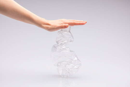 Close-up of a white people's hand crushing a crumpled plastic bottle in front of a white background