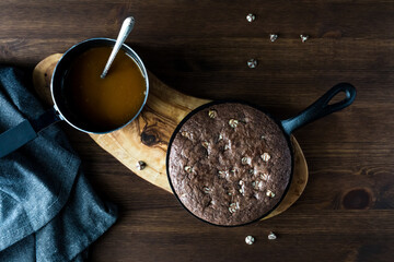 A top down view of a chocolate brownie baked in a small skillet with a mini pot of warm caramel sauce to spread on top.