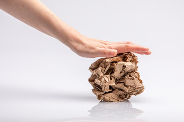 Close-up of a white people's hand crushing a crumpled piece of brown paper in front of a white background