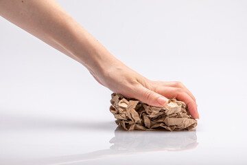 Close-up of a white people's hand crushing a crumpled piece of brown paper in front of a white background